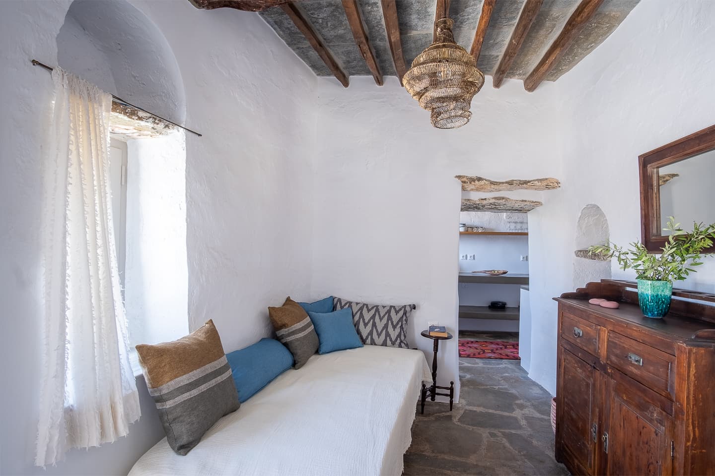 The living room daybed at Casa di Lavalle piled with cushions, beneath a woven pendant light and exposed timber ceiling.